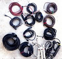 Collection of 6 power strips and multiple extension cords in various lengths arranged on floor surface.