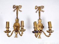 Pair of gold French style wall sconces mounted on a white background, showing front view with decorative bows and floral detail.