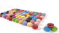 All 70 pieces of various colors of artificial French macaroons spread on a flat surface showing front angled side view.