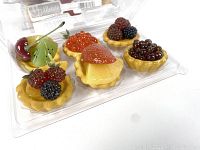 Close-up of six artificial fruit tarts inside clear plastic clamshell packaging, showing detailed artificial berries including cherry, kiwi, blackberries, and strawberry slice
