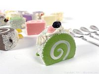 Close-up view of green artificial Swiss roll cake model decorated with black berry and cream details.