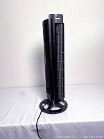 Front and angled front view of black Vornado tall tower fan showing vertical grille and circular base.