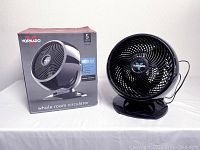 Black Vornado 7503 whole room air circulator fan with black base on white surface next to its box showing product and warranty information.