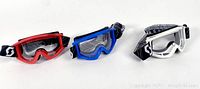 Front view of three ski goggles in red, blue, and white frames with clear lenses and black/white straps