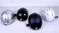 Four adult ski helmets side by side showing exterior colors and ventilation: black (2), silver, and white.