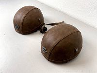 Two brown leather vintage-style half helmets with metal Woljay badge on front, seen from angled side view on white surface.