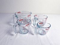 Set of four Pyrex measuring cups with handles and red measurement markings displayed on a white background.
