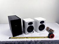 Frontal view of two white Audioengine speakers, black bass woofer, measuring tape and cables