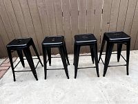 Front view of the 4 black metal bar stools arranged side by side showing the seating surface and legs.