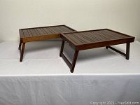 Two rectangular wooden breakfast trays with slatted tops and foldable legs displayed on white surface.