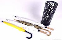 Four umbrellas laid flat with decorative umbrella holder placed standing beside them, showing size and color variety.