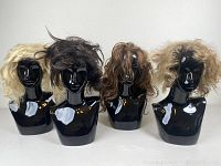 Front view of four wigs mounted on black mannequin heads, showing varying shades of blonde and brunette hair. Hair appears styled out of shape and voluminous.
