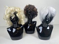 Three wigs displayed on black mannequin heads: blonde curly, black with brown highlights curly, and short white curly wig.
