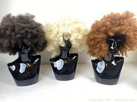 Front view of three afro wigs in dark brown, blonde and light brown colors displayed on black mannequin heads.
