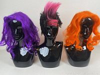 Front view image of three wigs on black mannequin heads: purple curly wig on left, pink and black mohawk wig center, bright orange curly wig right.