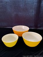 Front view of three Pyrex Daisy bowls arranged with the smallest two in front, showing yellow and orange exteriors with white interiors.