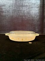 Photo of the Pyrex divided casserole on black background with a coin for scale, showing the side gold starburst Constellation pattern and clear lid