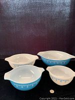Four Pyrex mixing bowls displayed on black fabric backdrop with a US quarter for scale