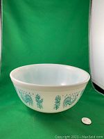 Side view of Pyrex Butterprint bowl showing folk art rooster and corn stalk design with coin for scale