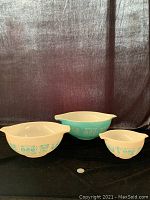 Set of 3 Pyrex Butterprint Cinderella bowls against a dark fabric backdrop, showing the full set and details of the turquoise Butterprint design on a white glass base.