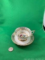 Porcelain cup and saucer set with daisy floral center under gold trim showing ornate gold details and decorative handle