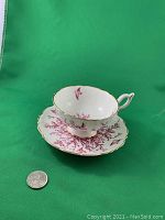 Front view of the tea cup on the saucer showing the pink birds in flight and branch pattern with gold trim.