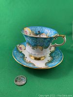 Front view of the Paragon bone china cup and saucer showing blue background with gold and floral rose designs, next to a quarter for scale.