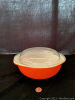 Front view of red round casserole dish with clear glass lid on top, quarter coin in front for scale