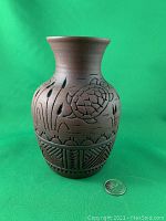 Front view of the brown pottery vase decorated with turtle and cattail carvings, with a US quarter coin for scale.