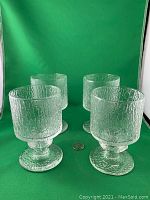 Front view of four clear textured glass goblets arranged with a coin for scale on green background.