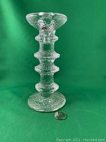 Front view of the textured glass candlestick next to a quarter for size reference against a green background.