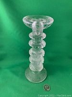 Front view of clear textured Iittala Festivo 5 ring candlestick with a quarter for scale, showing overall shape and size.