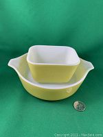 Two Pyrex pieces stacked: square fridge container inside round casserole dish, both chartreuse yellow with white interiors.