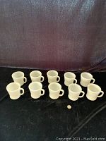Ten vintage Federal Glass milk glass mugs arranged in two rows on a black surface with a dark backdrop, quarter included for size reference.