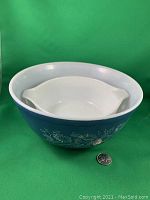 Photo showing smaller white-handled Pyrex casserole nested inside the larger 8.75-inch Pyrex bowl with Colonial Mist pattern against a green background, quarter coin for size reference.