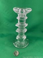 Full front view of the clear glass 4-ring Festivo candlestick with textured surface, placed on green background with a coin for scale.
