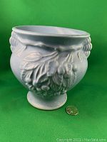 Front view of Nelson McCoy blue glazed pottery vase on green background, showing leaf and berry motif with size reference coin.