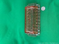 Pink Depression Glass Butter Dish with cube pattern shown on green background. Includes quarter for scale reference.