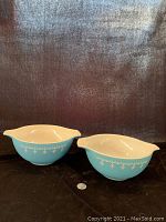 Pair of Pyrex Blue Snowflake Garland Cinderella Bowls with a quarter for size reference, showing the exterior blue pattern with white snowflakes.