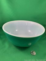 Green Pyrex bowl with white interior shown from top angle with a quarter for size reference, displaying the bowl's interior and rim.