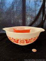 Large white glass cinderella bowl with orange/red birds and flowers pattern labeled as Pyrex Friendship pattern beside a penny for size.