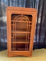 Front view of the 1940's wooden cabinet showing decorative front grid with broken section and no glass panel inside.
