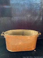 Front view of the oval copper firewood/coal bin with handles, showing dents and patina on the surface.