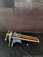 Side angle view of the blue cast metal woodworking vise showing jaws, handle and threaded rods.