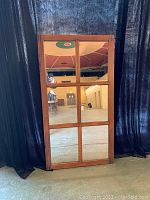 Full view of the 6 pane window frame mirror leaning against a black curtain background, showcasing the rectangular shape and wooden frame with visible grain and slightly worn finish.