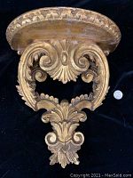 Front view of Florentine carved wood wall shelf showing decorative scroll and leaf motifs with half-moon shelf surface, showing wear.