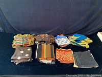 Top view showing several folded silk scarves in various patterns and colors arranged on a black surface.
