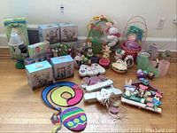 Full lot display on wood floor showing multiple Easter themed items including boxed water globes, plush bunny decorations, colorful wooden and plastic Easter eggs, baskets, and various small figurines and votives.