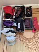 Photo shows assorted belts in bins, wallets, hats on floor including Callaway golf hats, purple evening bag