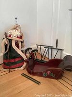 Santa figurine seated with red and green robe trimmed in beige fur, holding lantern and staff beside unassembled red sleigh and metal runners on floor.